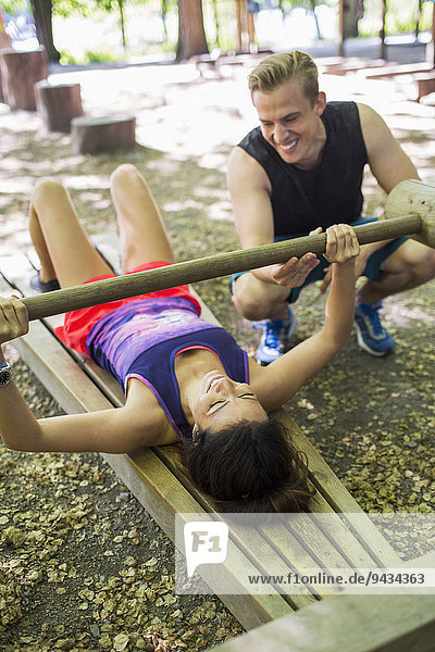 Mann hilft Frau beim Heben von Holzgewicht im Fitnessstudio im Freien
