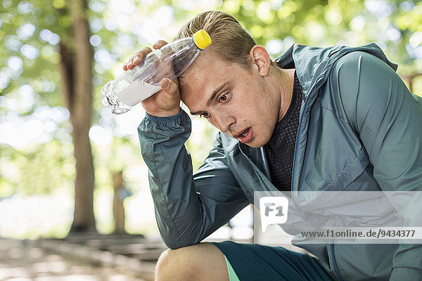 Müder Mann keucht  während er nach dem Training im Park die Wasserflasche hält.