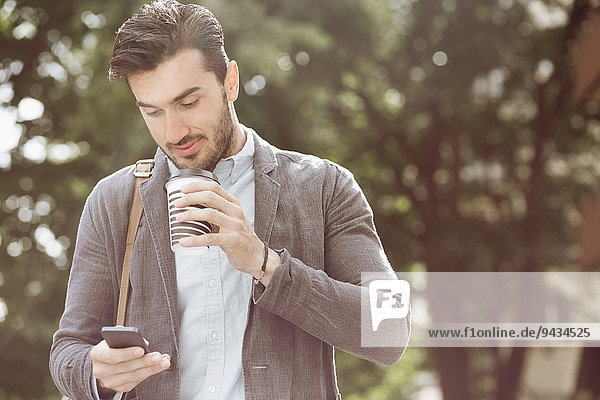 Young businessman having coffee while using smart phone outdoors