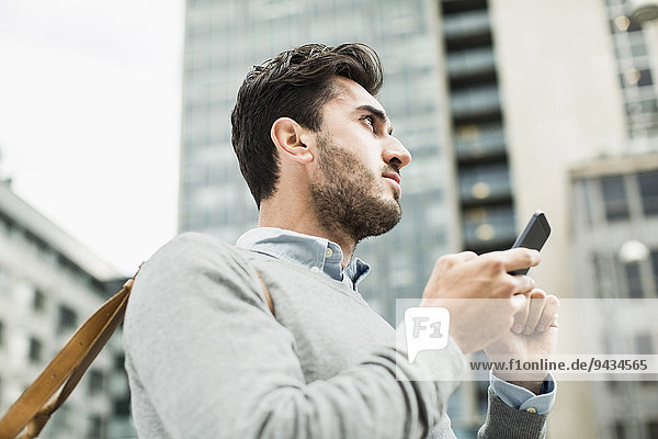 Low angle view of businessman looking away while holding smart phone against building