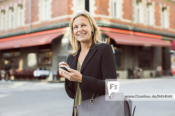 Glückliche Geschäftsfrau schaut weg  während sie das Handy in der Stadt benutzt.