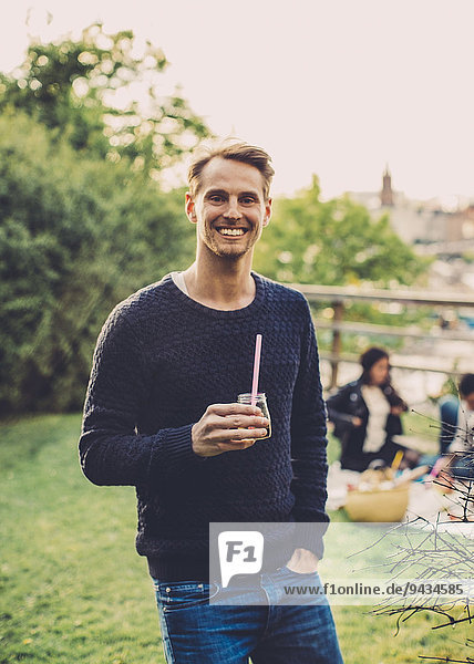Porträt eines glücklichen Mannes mit Holunderblütengetränk bei einem Picknick auf dem Dach mit Freunden.
