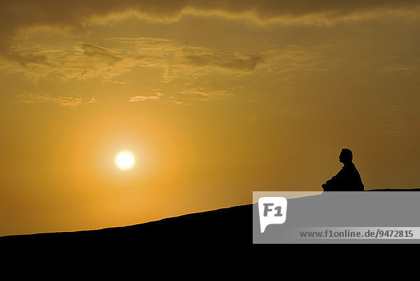 Ein Buddhist meditiert bei Sonnenuntergang