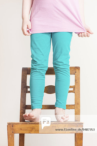 Kleines Mädchen  4 Jahre  steht mit nackten Füßen auf einem kleinen Holzstuhl