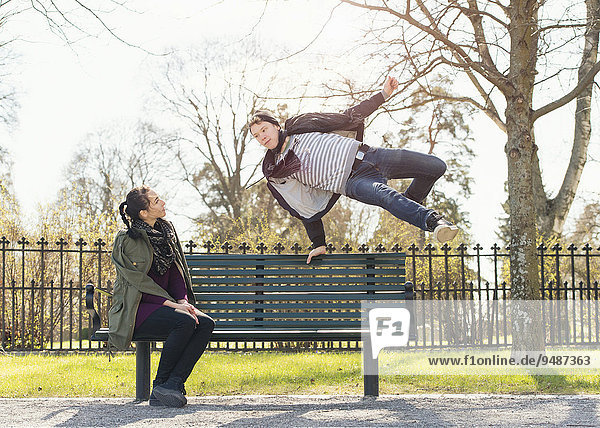 Ein junger Mann versucht  ein gleichgültiges Mädchen mit einem Sprung über eine Parkbank zu beeindrucken  Schweden  Europa