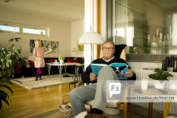 Senior man reading book  granddaughter on background