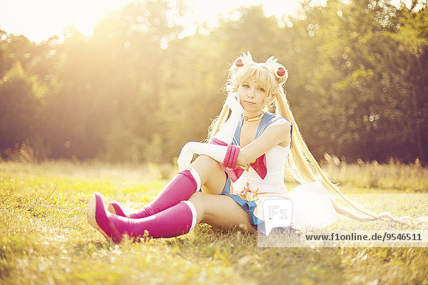 Frau im Kostüm von Pretty Guardian Sailor Moon sitzend auf einer Wiese
