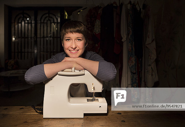 Porträt einer lächelnden Modedesignerin  die sich in ihrem Atelier auf die Nähmaschine stützt.