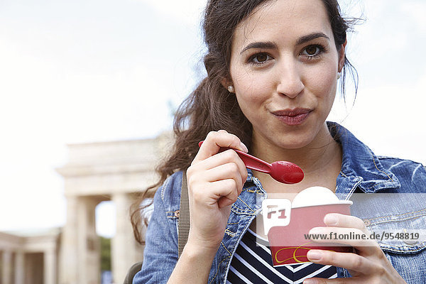 Germany  Berlin  portrait of young female tourist eating ice cream near Brandenburg Gate