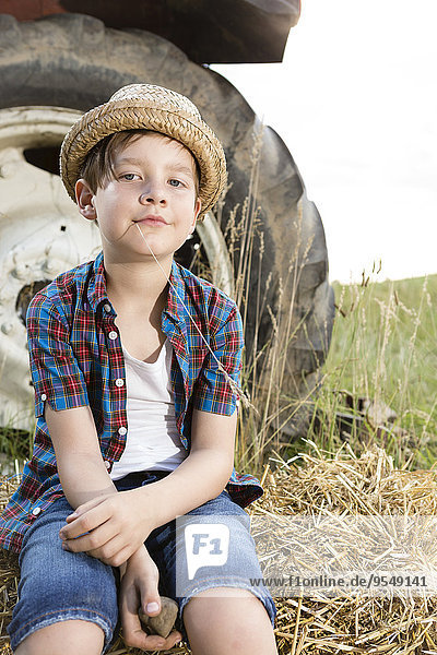 Portrait of smiling little boy sitting on a straw bale wearing straw hat