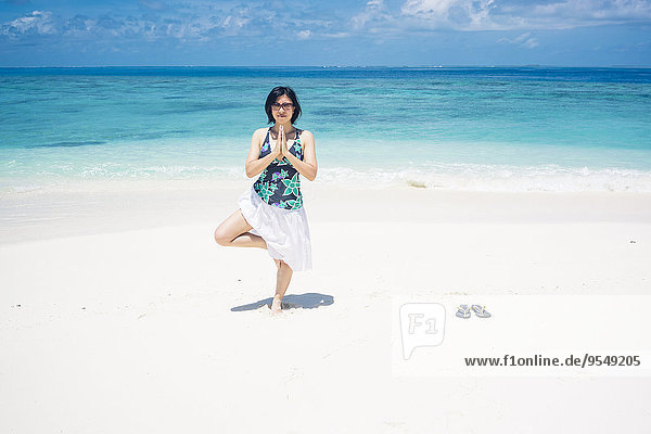 Malediven  Ari Atoll  junge Frau beim Yoga am Strand