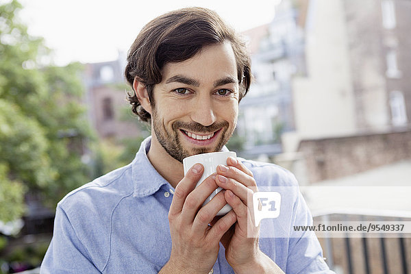 Porträt eines lächelnden Mannes auf dem Balkon beim Kaffeetrinken