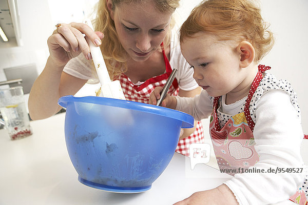 Mother and little daughter baking cake together in their kitchen