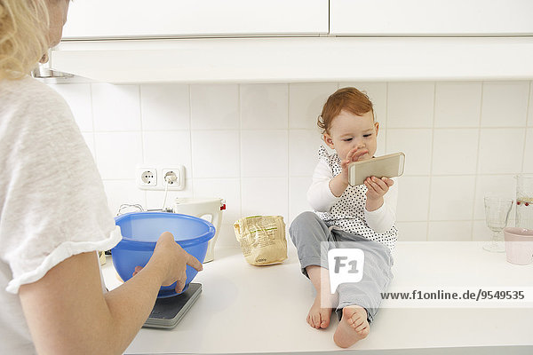 Little girl sitting on kitchen counter with smartphone
