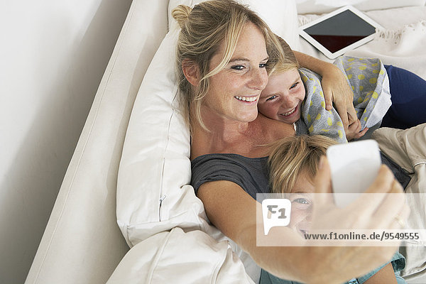 Glückliche Mutter Tochter und Sohn auf der Couch die einen Selfie nehmen.