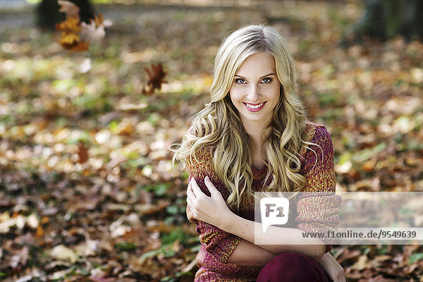 Porträt einer lächelnden blonden Frau mit Strickpullover im Herbstwald