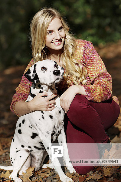 Portrait of smiling blond woman with Dalmatian in autumnal forest