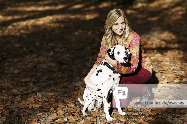 Smiling blond woman with Dalmatian in autumnal forest