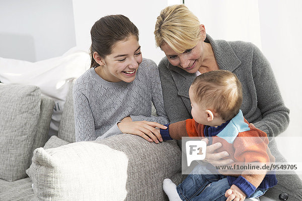 Mutter sitzend mit Tochter und Baby auf der Couch  lächelnd