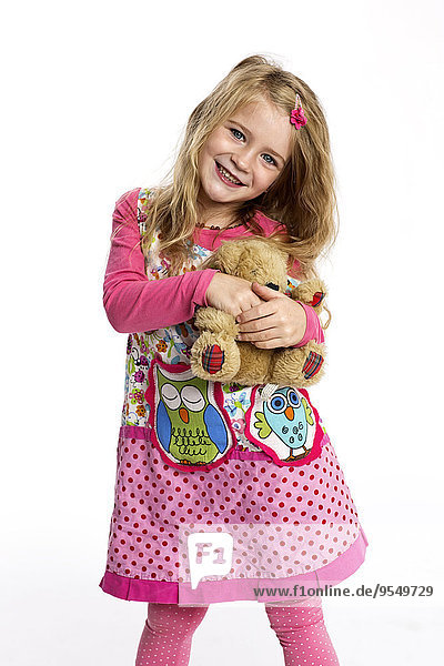 Porträt eines fröhlichen kleinen Mädchens mit ihrem Teddybären im bunten Kleid vor weißem Hintergrund.