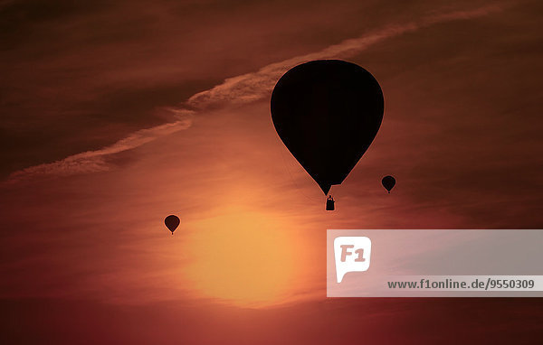 Silhouetten von drei Luftballons vor rotem Abendhimmel