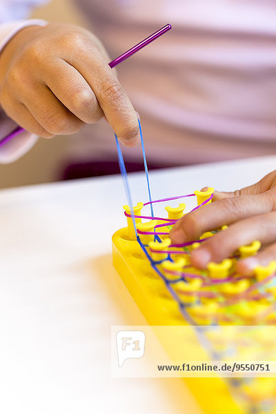 Kleine Mädchenhände machen Armbänder mit Webbrett
