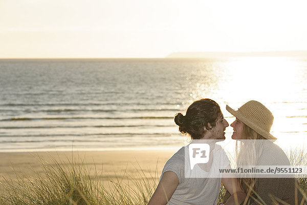 Junges Paar sitzt an Stranddünen vor dem Atlantik