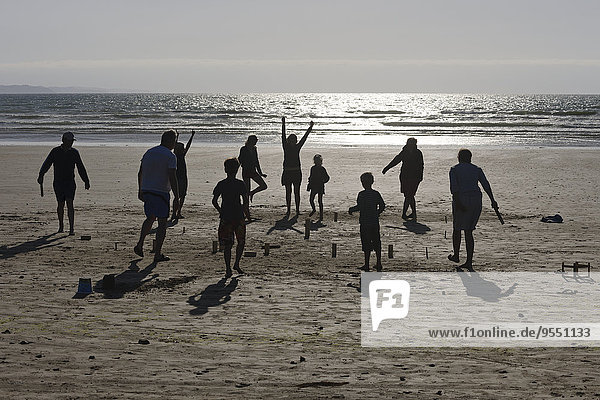 Zwei Gruppen spielen Kubb am Strand in der Abenddämmerung.