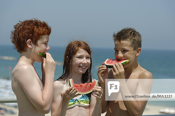 Italy  girl and two teenage boys eating watermelon slices at the beach