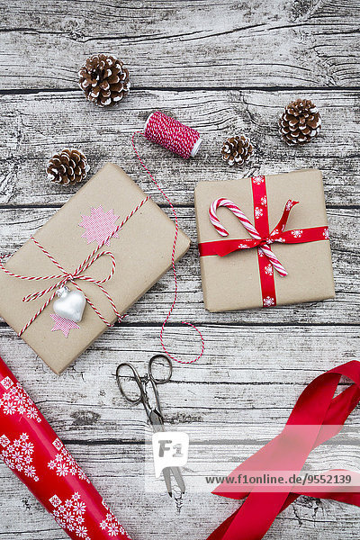 Verpackte Weihnachtsgeschenke,  Tannenzapfen,  Band und Schere auf Holz