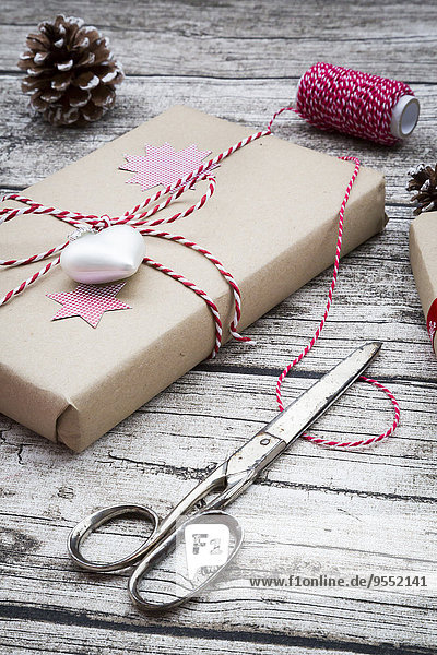 Verpackte Weihnachtsgeschenke,  Scheren,  Bänder und Tannenzapfen auf Holz