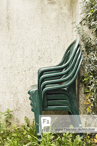 Stack of green garden chairs placed next to a wall