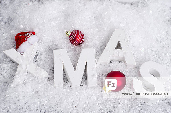 Rote Weihnachtskugeln und weiße Buchstaben,  die das Wort'XMAS' bilden,  das im Kunstschnee liegt.