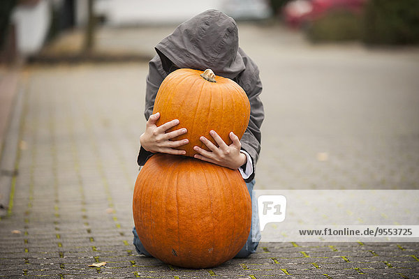 Boy kneeling behind two big pumpkins