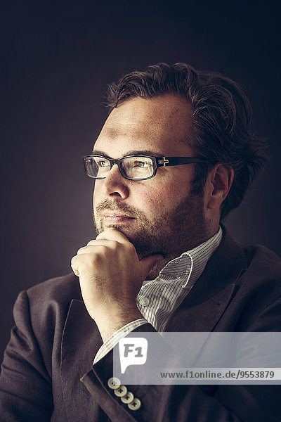 Porträt eines nachdenklichen Mannes mit Vollbart und Brille vor dunklem Hintergrund