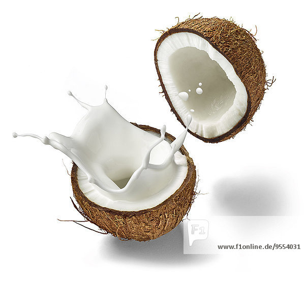 Zwei Hälften einer Kokosnuss und spritzende Kokosmilch vor weißem Hintergrund