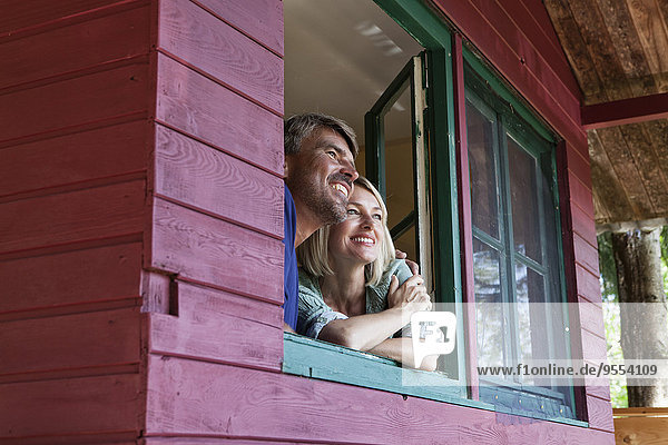 Happy mature couple looking out of window of summer house