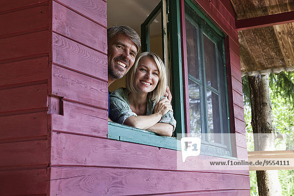 Happy mature couple looking out of window of summer house