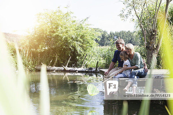 Glückliche Familie sitzend mit Dip-Netz am Steg am See