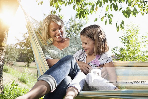Happy mother and daughter sitting in hammock