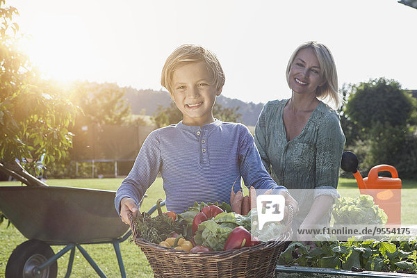 Boy with mother in garden carrying basket with vegetables