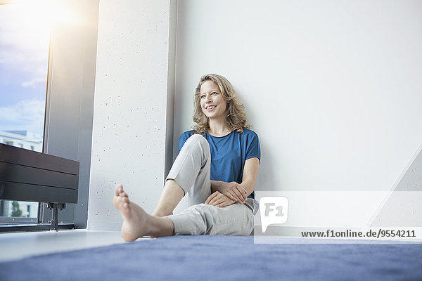 Porträt einer lächelnden reifen Frau  die in ihrer Wohnung auf dem Boden sitzt.