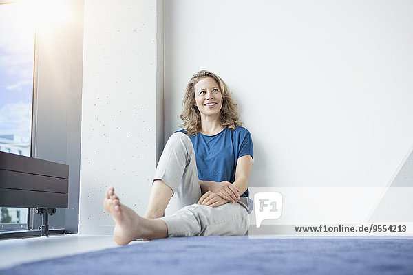 Porträt einer lächelnden reifen Frau  die in ihrer Wohnung auf dem Boden sitzt.