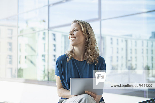 Lächelnde reife Frau mit digitalem Tablett sitzend in ihrer Wohnung