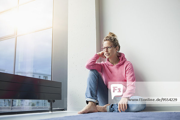 Reife Frau sitzt auf dem Boden in ihrer Wohnung und schaut durchs Fenster.