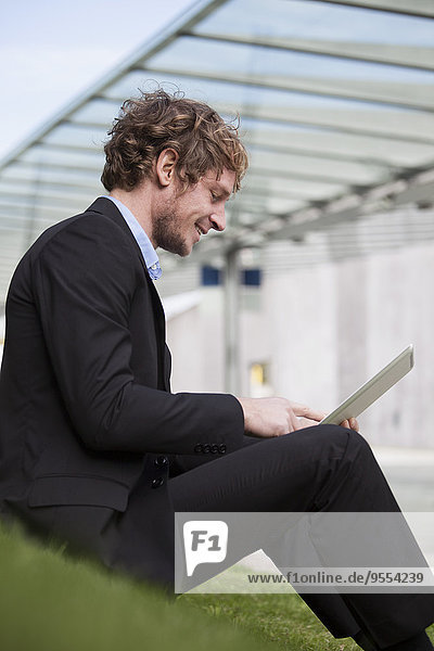 Businessman sitting on a meadow with his digital tablet