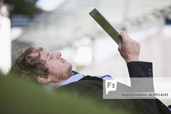 Businessman lying on a meadow using his digital tablet