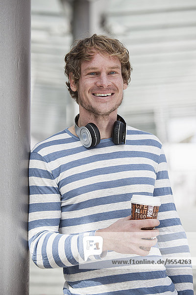 Portrait of smiling man with headphones and coffee to go