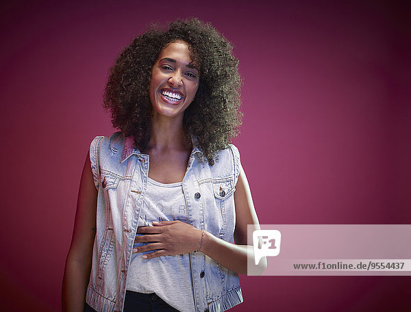 Porträt einer lachenden jungen Frau mit Afro vor rotem Hintergrund