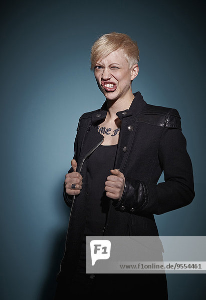 Porträt einer aggressiven jungen blonden Frau in Schwarz vor blauem Hintergrund